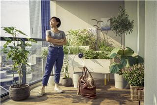 une femme debout à côté des plantes de son appartement avec un sac de voyage plein à craquer