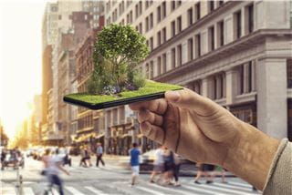 A hand holding a smartphone in a busy street, that has a small garden coming out of it.