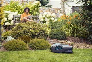 A man reading while his robotic lawnmowers is doing the work