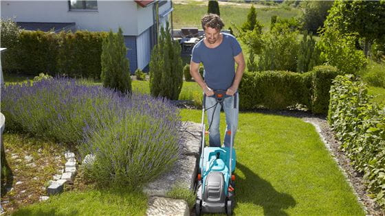 A man mowing his lawn right next to a stone wall