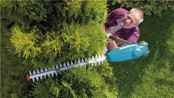 A man trimming the top of a hedge with the Gardena Hedge Trimmer