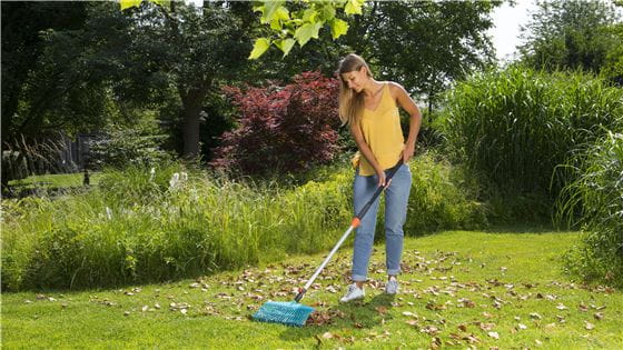 A woman raking leaves on a lawn with a Gardena combisystem product
