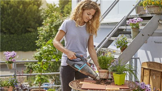 A woman using the Gardena EasyClean Vacuum to clean up soil on her balcony
