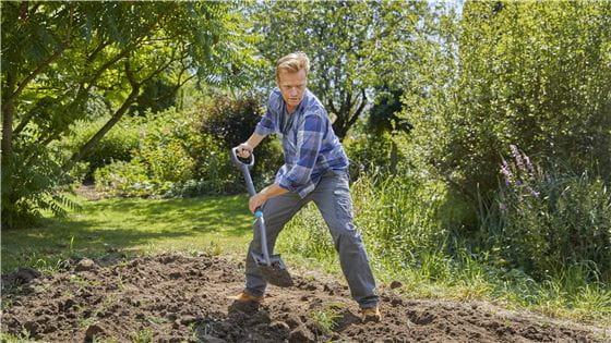 A man digging up a garden with a Gardena spade