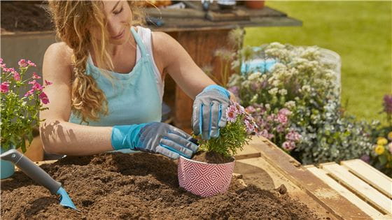A woman planting flowers into a pot while wearing Gardena Gloves