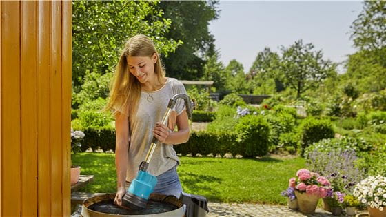 Young woman installing a Rain Water Tank Pump in a barrel in her garden
