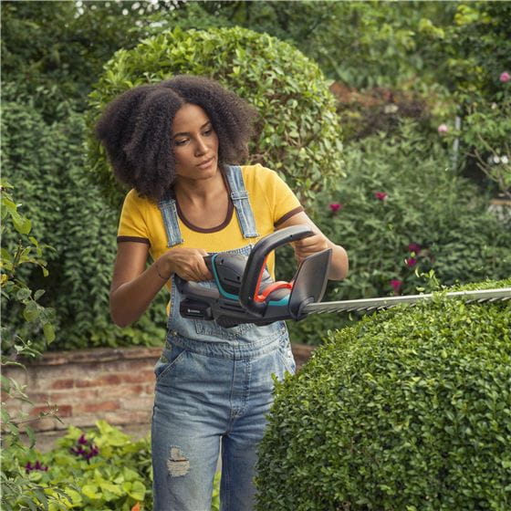 A woman using a battery hedge trimmer in her garden